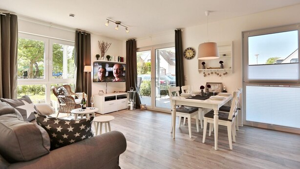Ein modernes Wohnzimmer mit einer Couch, einem Esstisch für vier Personen und einem an der Wand befestigten Fernseher.