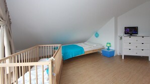A bedroom with a bunk bed, a small bedside table with a lamp, a dresser, and a television on a stand.