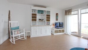 A living room with a white cabinet, a television, a rocking chair, and a large window.