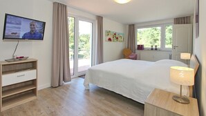 Un dormitorio con cama, televisor, escritorio, silla y ventana.