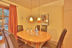 A round wooden dining table with four chairs, a bottle of wine, and two small potted plants.