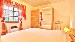 A bedroom with a large bed, a wardrobe, a mirror, and a window with curtains.