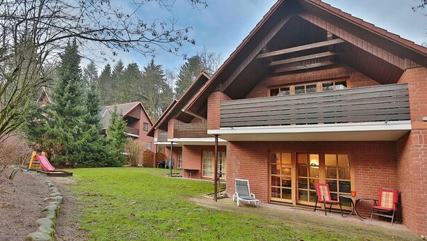 A two-story brick house with a covered patio area and a small deck.