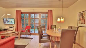 A dining area with a wooden table and chairs, a television, and a window with curtains.