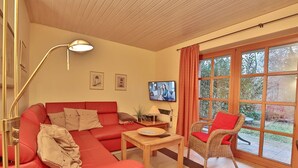 A cozy living room with a red sofa, a wicker chair, a wooden coffee table, and a TV on the wall.