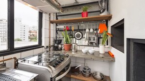 Cocina compacta con estufa a gas, cafetera y distintos utensilios en la pared.