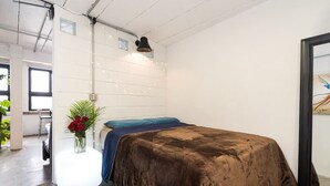Un dormitorio con una colcha marrón, una almohada azul y un jarrón con flores rojas sobre una mesa blanca.