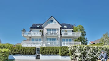 Ein mehrgeschossiges Wohngebäude mit Balkonen, einem verschlossenen Eingang und einer gepflegten Hecke.