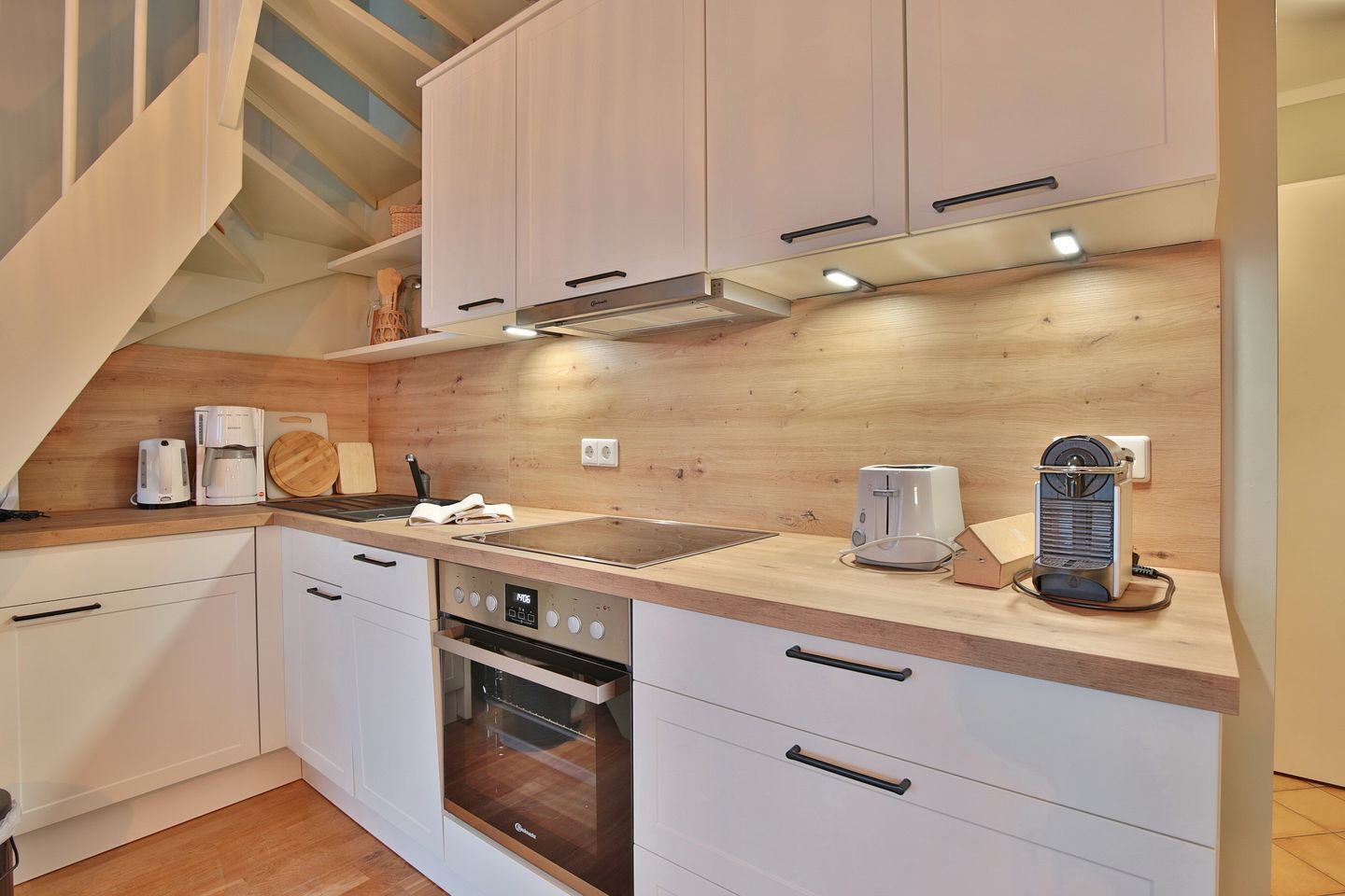 A modern kitchen with white cabinets, a wooden countertop, a built-in oven, a coffee maker, and a toaster.
