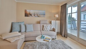 A living room with a beige sofa, patterned cushions, a round coffee table, and a painting on the wall. - Seerose II Apartment 14 - House Seerose (Scharbeutz)