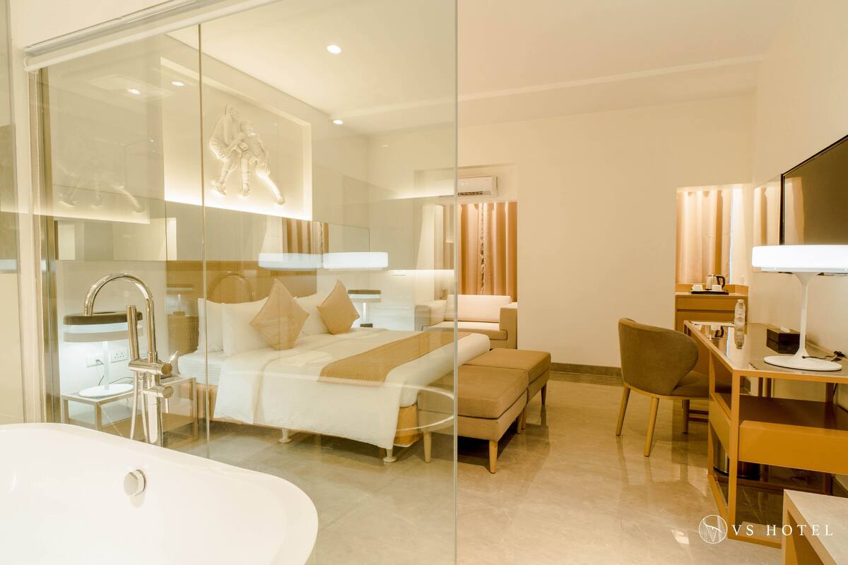 Una habitación de hotel moderna con cabina de ducha de vidrio, una cama grande con cabecero, un escritorio con silla y un televisor de pantalla plana.