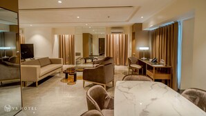 A modern hotel room with a sofa, armchairs, a marble table, and a desk with a lamp. - VS Hotel (Quezon City)
