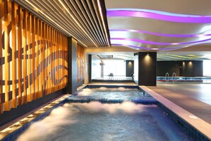 Un espace spa moderne doté d’un jacuzzi, de panneaux muraux en bois et d’un plafond éclairé de lumières violettes.