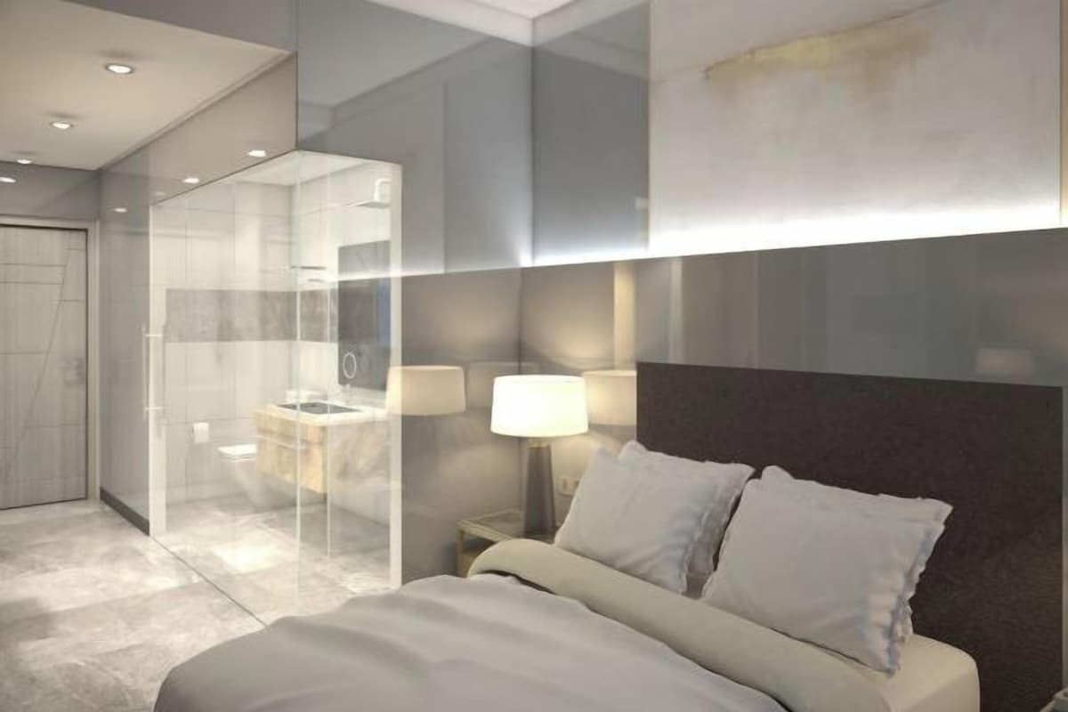 Une chambre d’hôtel moderne avec un grand lit, une douche en verre et une table de chevet avec une lampe.