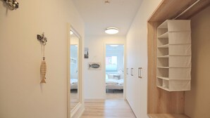 Un pasillo estrecho con suelo de madera, una pared blanca con un adorno de pez y una puerta que da a un dormitorio.