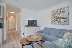 Un salon moderne avec un canapé gris, une table basse en bois et un téléviseur posé sur un meuble blanc.