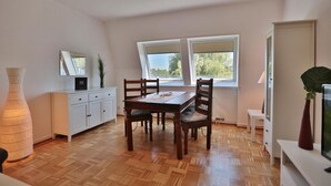 A dining area with a wooden table and chairs, a white cabinet, and a large window providing natural light. - Domizil Seestraße - Ihr Domizil Seestraße (Scharbeutz)
