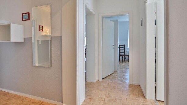 A hallway with a wooden floor, white walls, and a door leading to a dining area. - Domizil Seestraße - Ihr Domizil Seestraße (Scharbeutz)