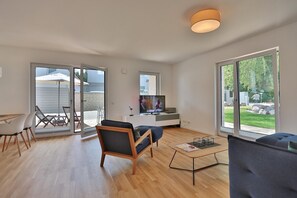 A modern living room with a TV, a sofa, a coffee table, and a dining area with chairs and a table.