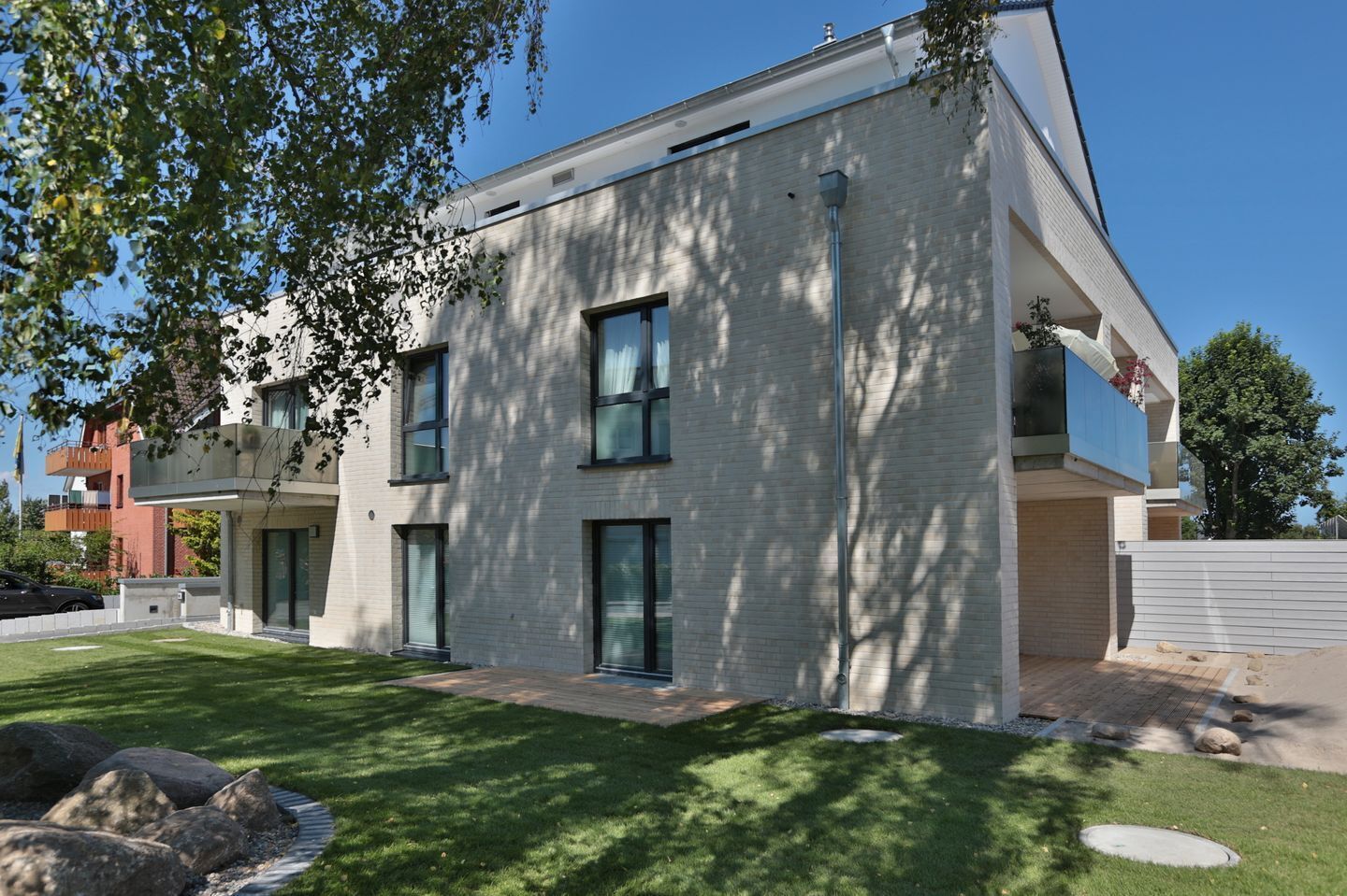 Een modern gebouw met twee verdiepingen, een plat dak, grote ramen en een verzorgd gazon met stenen.