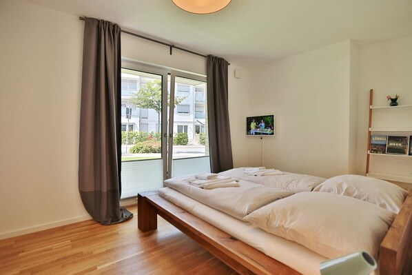 A bedroom with a bed, a bench, a TV, and a view of a building outside.