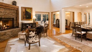 Un intérieur spacieux agrémenté d’une cheminée en pierre, d’un coin repas avec une grande table et des chaises, et d’un espace salon confortable avec une autre cheminée.