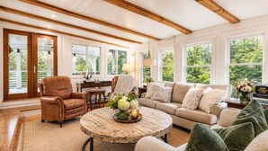 Un salon spacieux avec un plafond en bois, de grandes fenêtres, un fauteuil en cuir, un canapé et une table basse ronde.