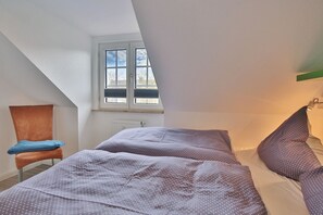 Quarto com duas camas, uma cadeira e uma janela.