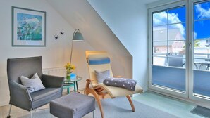 A modern loft bedroom with a large skylight, a cozy seating area with a chair and ottoman, and a framed painting on the wall.