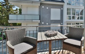 Ein Balkon mit Korbstühlen und einem Tisch, mit Blick auf eine Straße und ein Gebäude im Hintergrund.