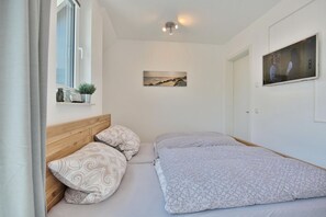 A bedroom with a wooden headboard, two beds with patterned bedding, a window with a view, a painting on the wall, and a television on the right.