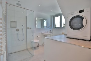 Ein modernes Badezimmer mit einer Duschkabine, Toilette, Waschbecken und einer integrierten Waschmaschine.