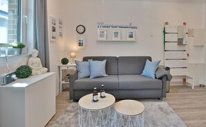 Un salon moderne avec un canapé gris, deux petites tables rondes, un meuble blanc et une petite statue.