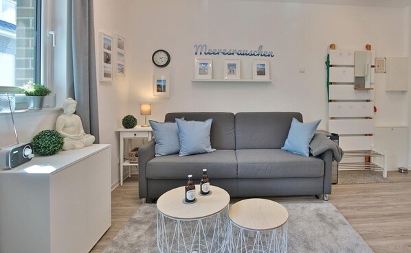 A modern living room with a grey sofa, two round coffee tables, a white cabinet, and a small statue.