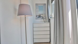 A hallway with a floor lamp, a white dresser, and a window with curtains. - Bude 37 Apartment 6 - Bude 37 (Scharbeutz)