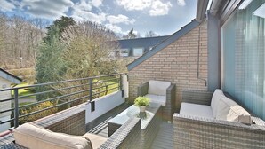 A balcony with wicker furniture and a potted plant, overlooking a residential area and trees. - Haus Adria Appartement 31 - Haus Adria (Scharbeutz)