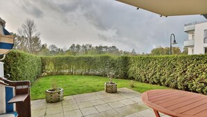 Eine Terrasse mit Tisch und Stühlen, ein kleiner Garten mit Topfpflanzen und ein Heckenstreifen.