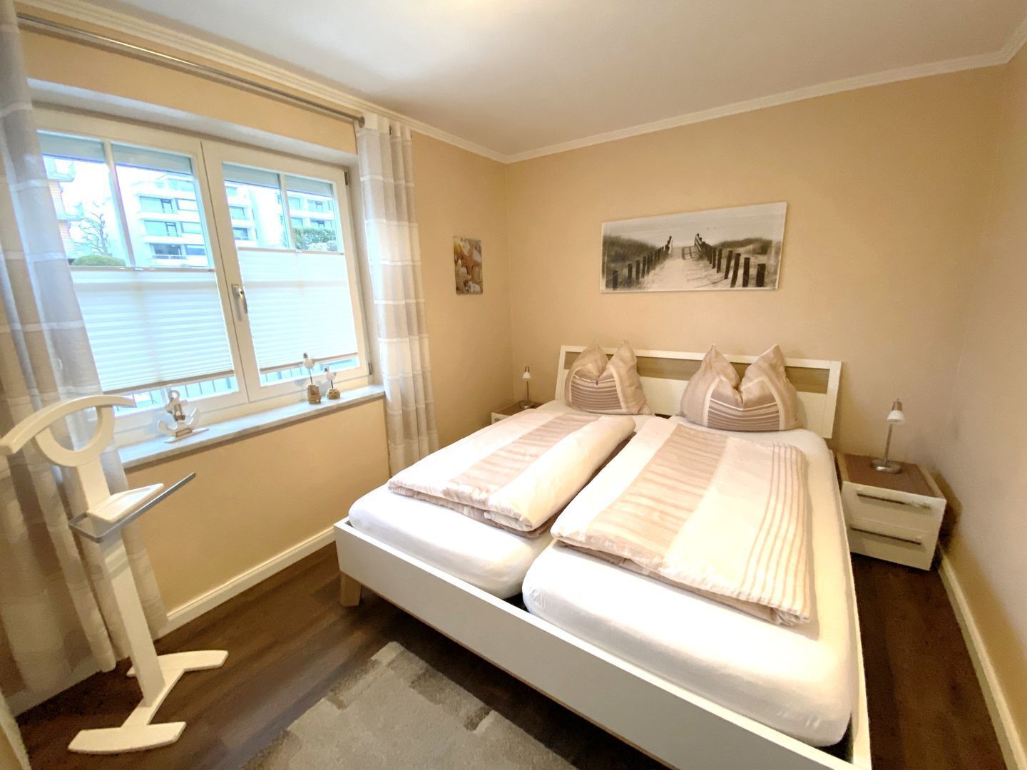 Une chambre à coucher avec un grand lit, une fenêtre avec des stores, une table de chevet avec une lampe et un tableau accroché au mur.