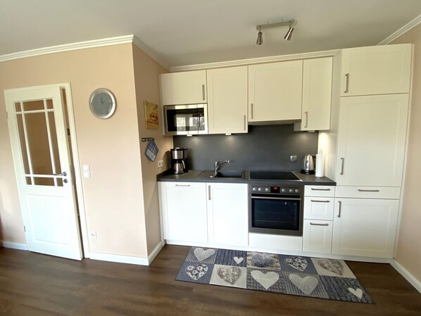 A compact kitchen with white cabinets, a microwave, a stove, and a sink.
