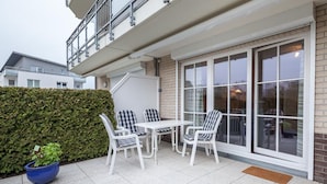 A patio with a table and chairs, a blue planter, and a hedge.