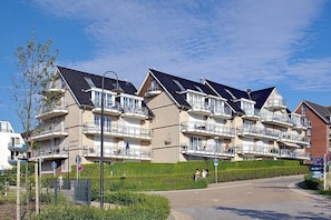 A row of modern multi-story residential buildings with balconies, a paved pathway, and a clear blue sky.