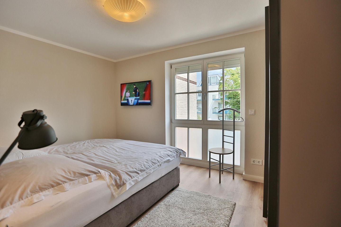 A bedroom with a bed, a desk, a chair, and a window.