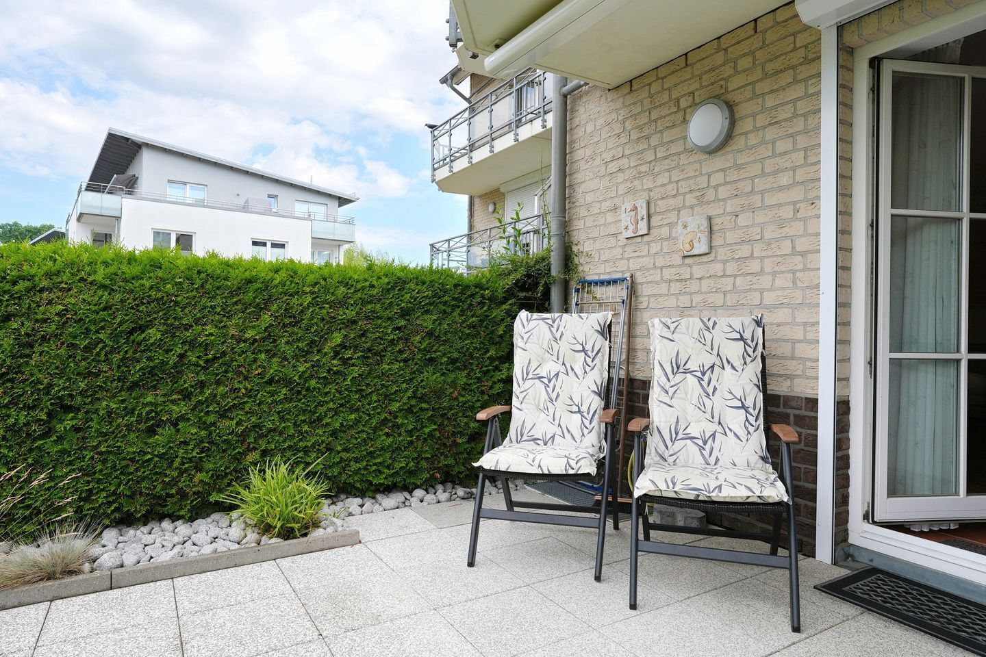 Zwei Stühle mit Blattmuster vor einem Gebäude mit Ziegelwand und Balkon.