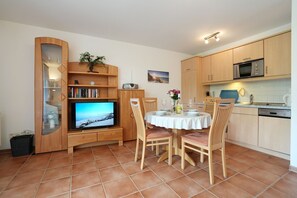 A compact living space with a TV, dining table, chairs, and a kitchen area.