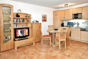 Un espacio habitable compacto con televisor, armarios de madera, zona de comedor y cocina.