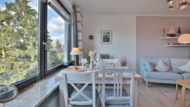 A modern living room with a dining area, large windows, and a view of trees.