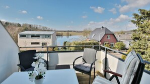 A balcony with a table, chairs, and a view of a lake and houses.