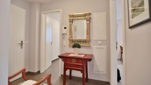 Un pasillo con un banco de madera, un espejo con marco decorativo y una puerta con interruptor de luz.