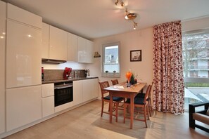 Una cocina moderna con armarios blancos, una mesa de comedor con sillas y un ventanal con cortinas.