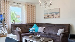 Ein Wohnzimmer mit einem braunen Sofa, einem Couchtisch, einem Bild von Vögeln am Strand und einer Chandelier.
